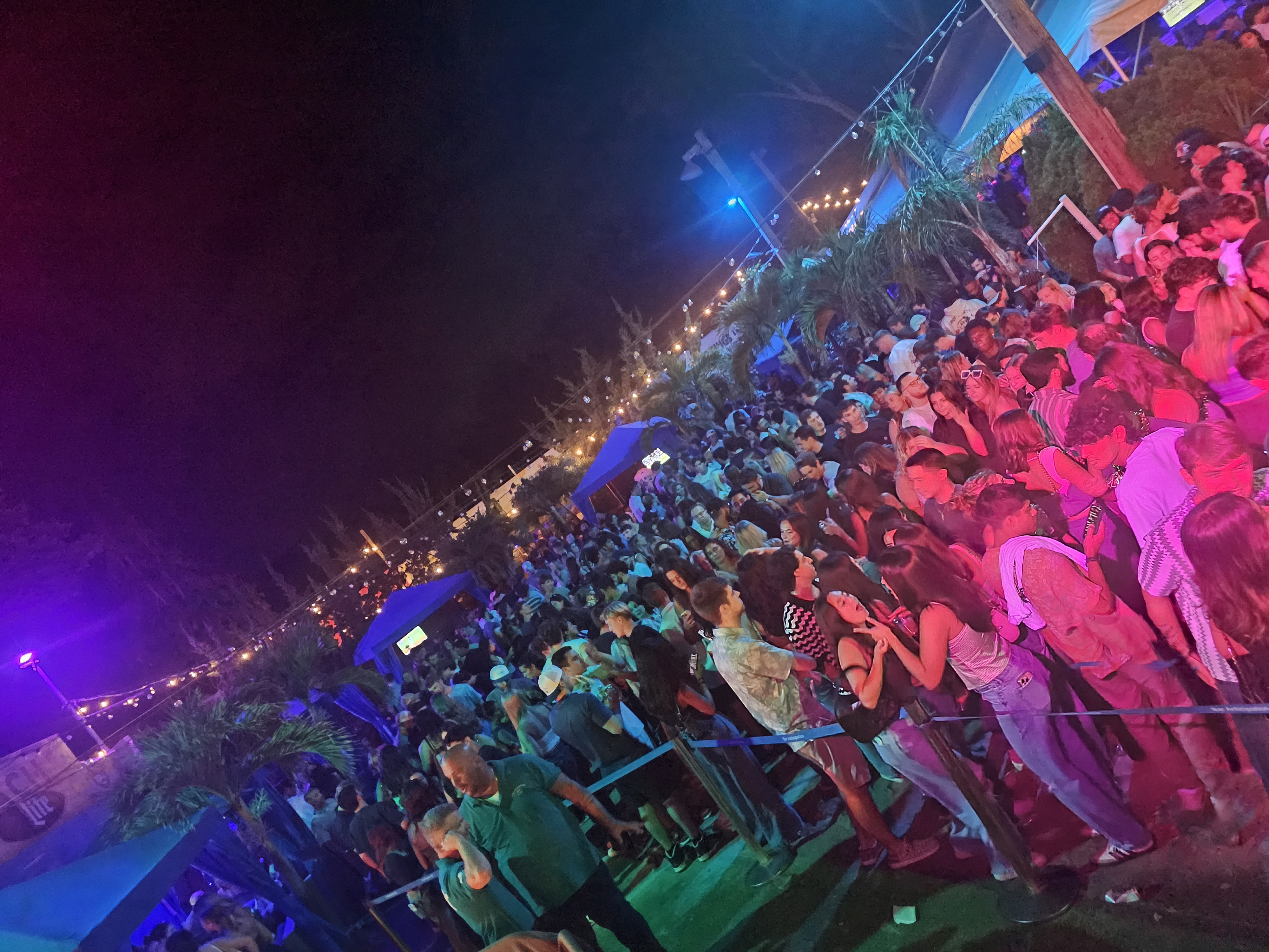 Wide shot of an outdoor night crowd, stage lights overhead