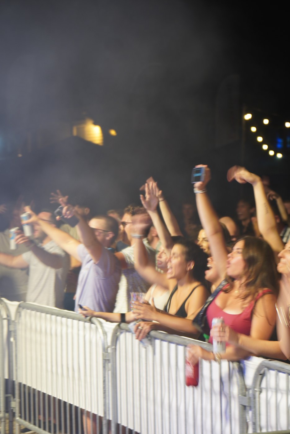 Crowd with hands up at the rail at Bar A, faces lit