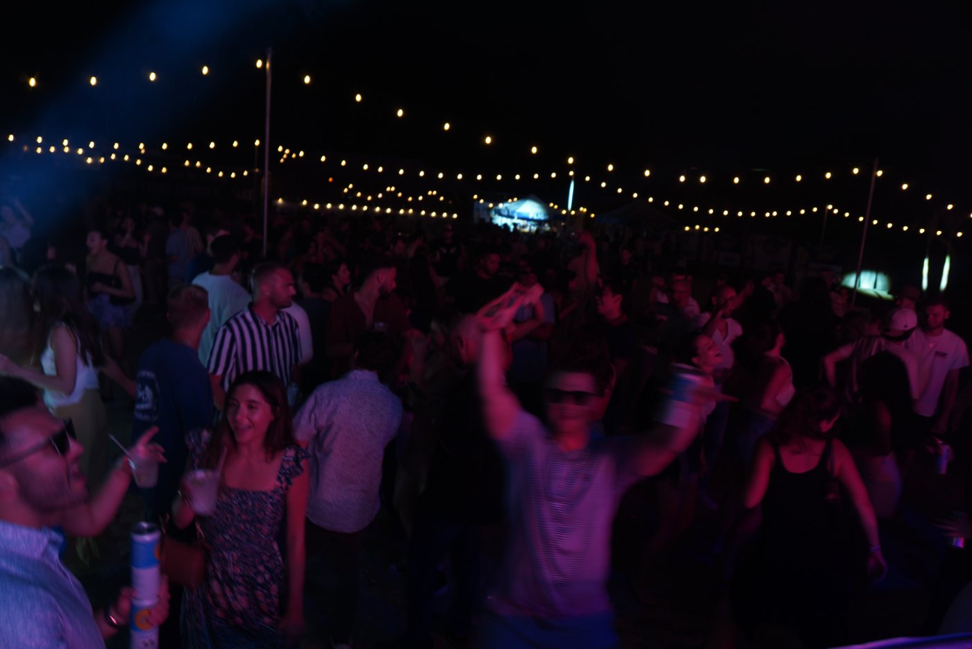 A big beach-party crowd under string lights at Bar A