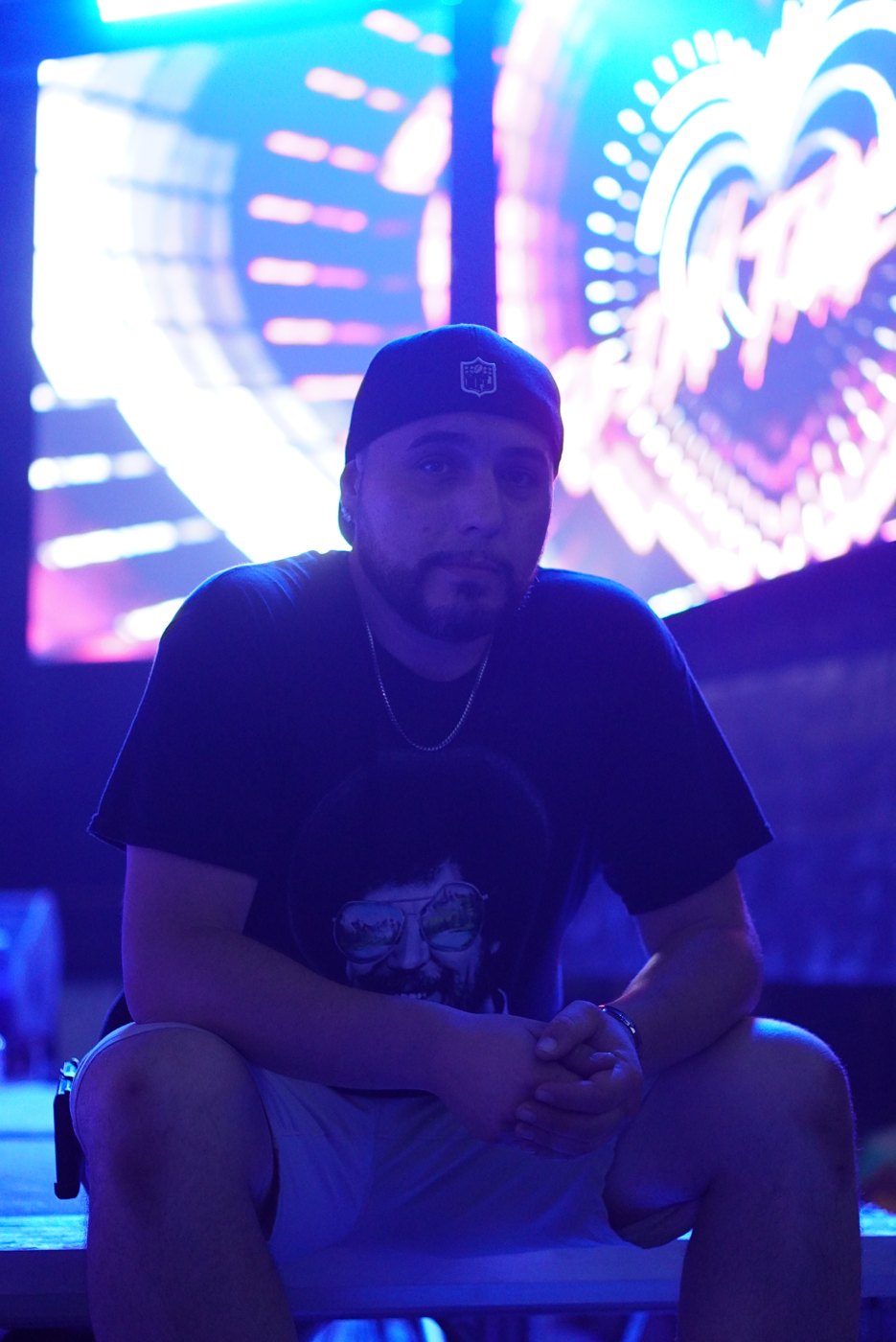 Barry seated at the Bar A booth in blue light with a glowing heart visual behind him