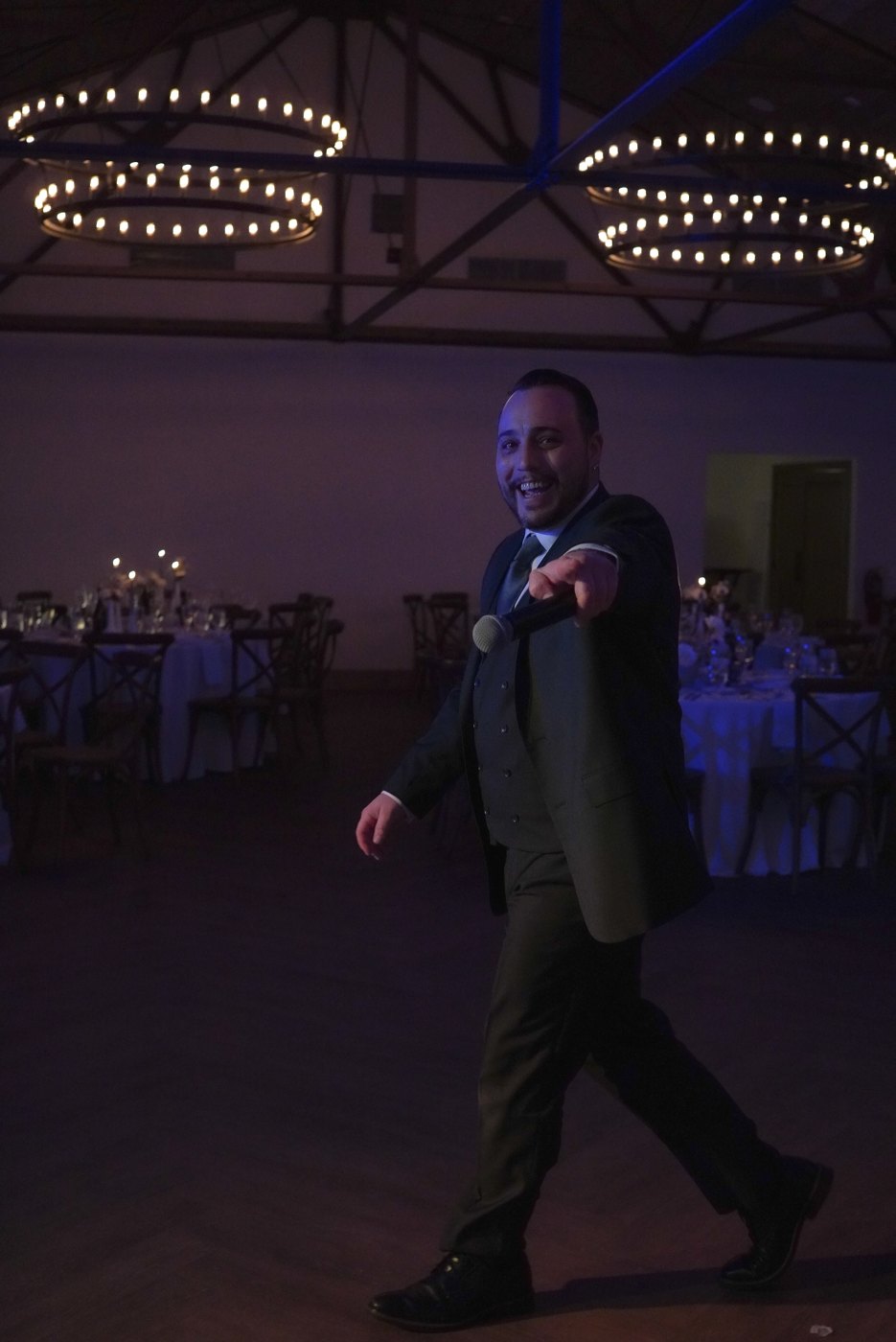 Barry in a suit pointing across the dance floor under blue uplighting