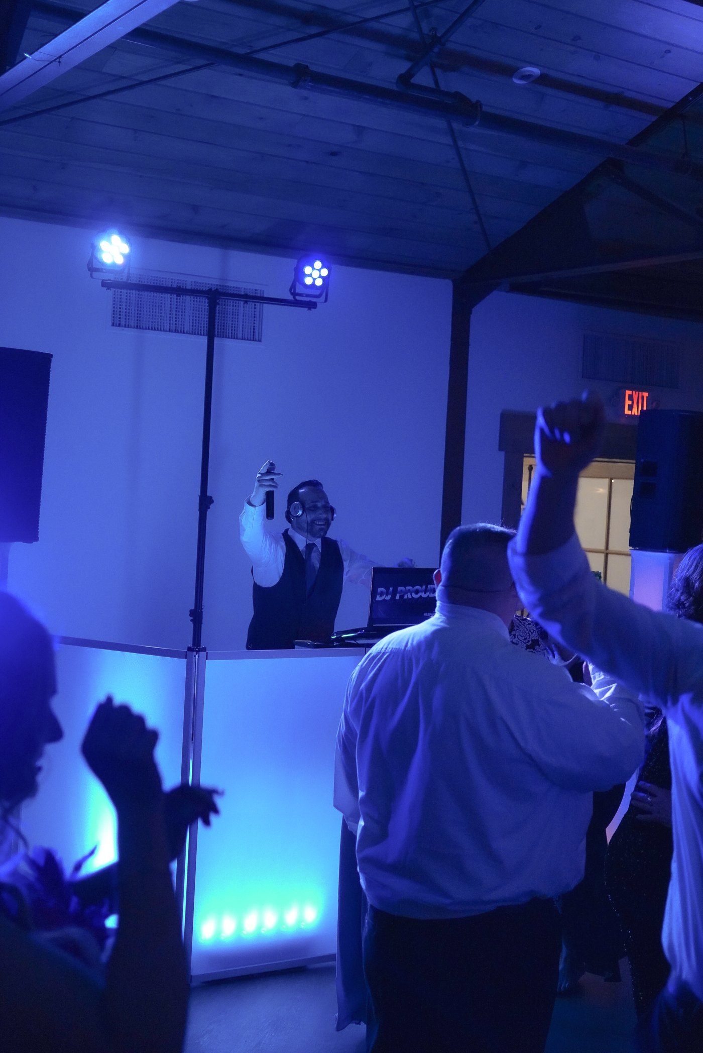 Barry on the microphone at the glowing white DJ facade, blue uplighting, guests dancing