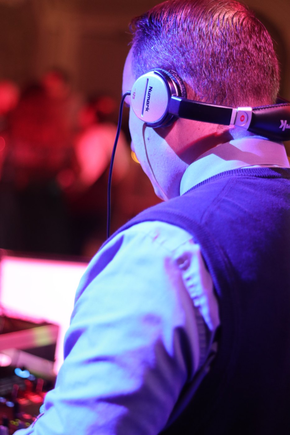 Close-up of Barry with headphones on at the decks, lit in blue and pink