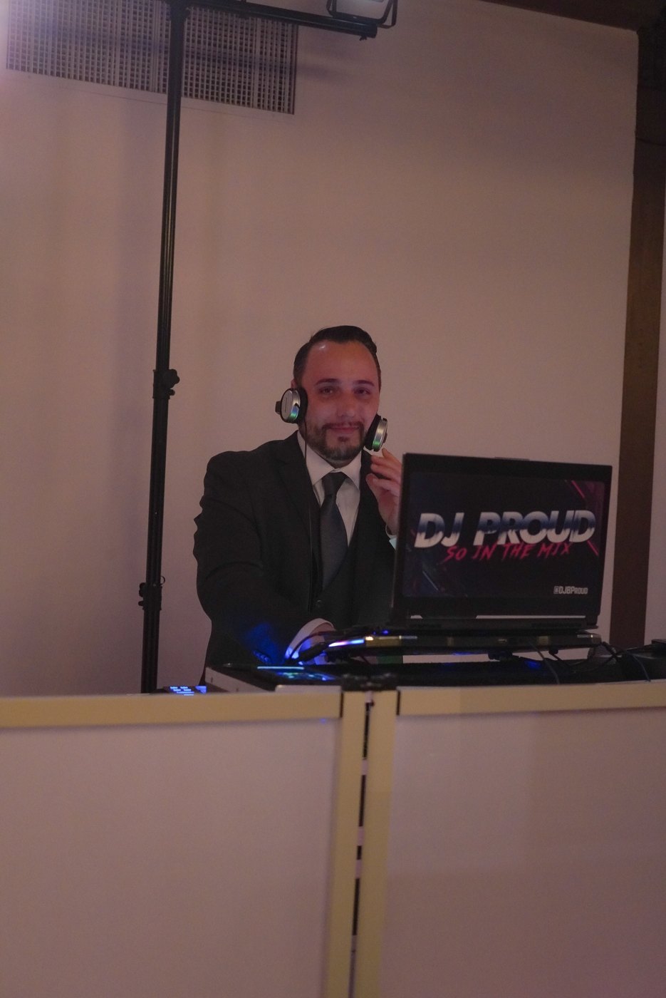 Barry with headphones at the booth — laptop screen reads DJ PROUD SO IN THE MIX