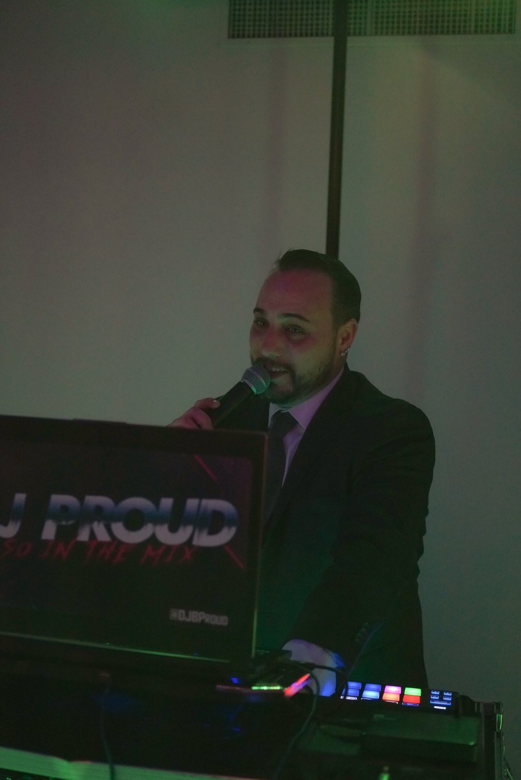 DJ Barry Proud in a suit at the booth, microphone in hand