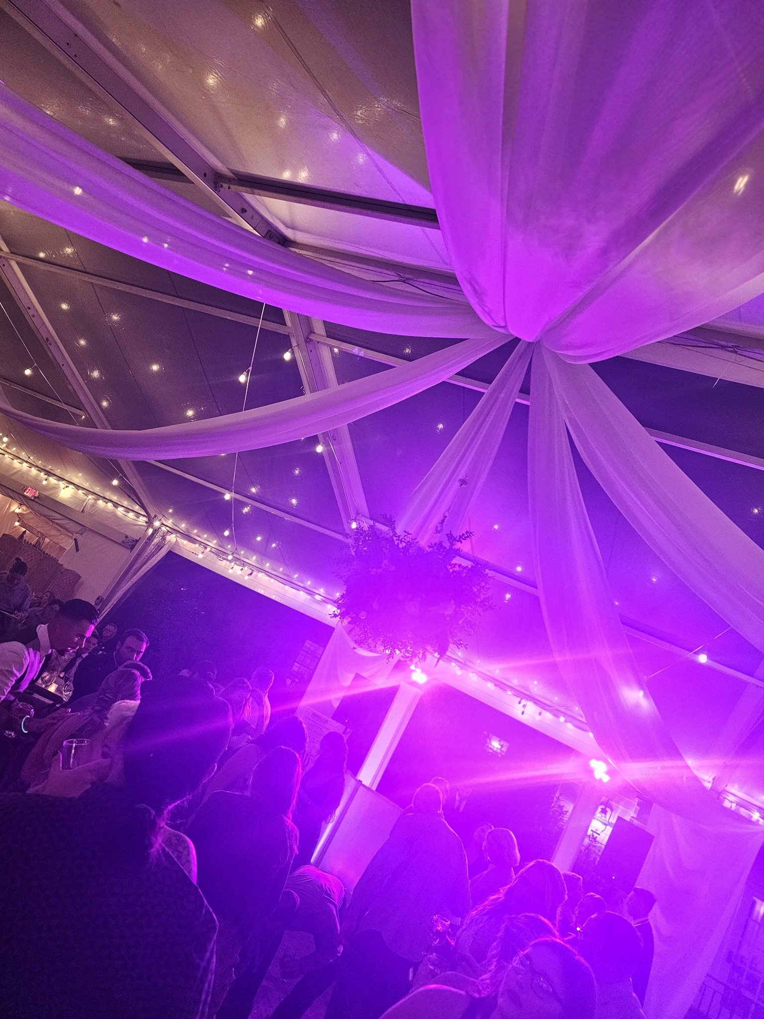 Wedding guests dancing under purple uplighting and string lights in a tent