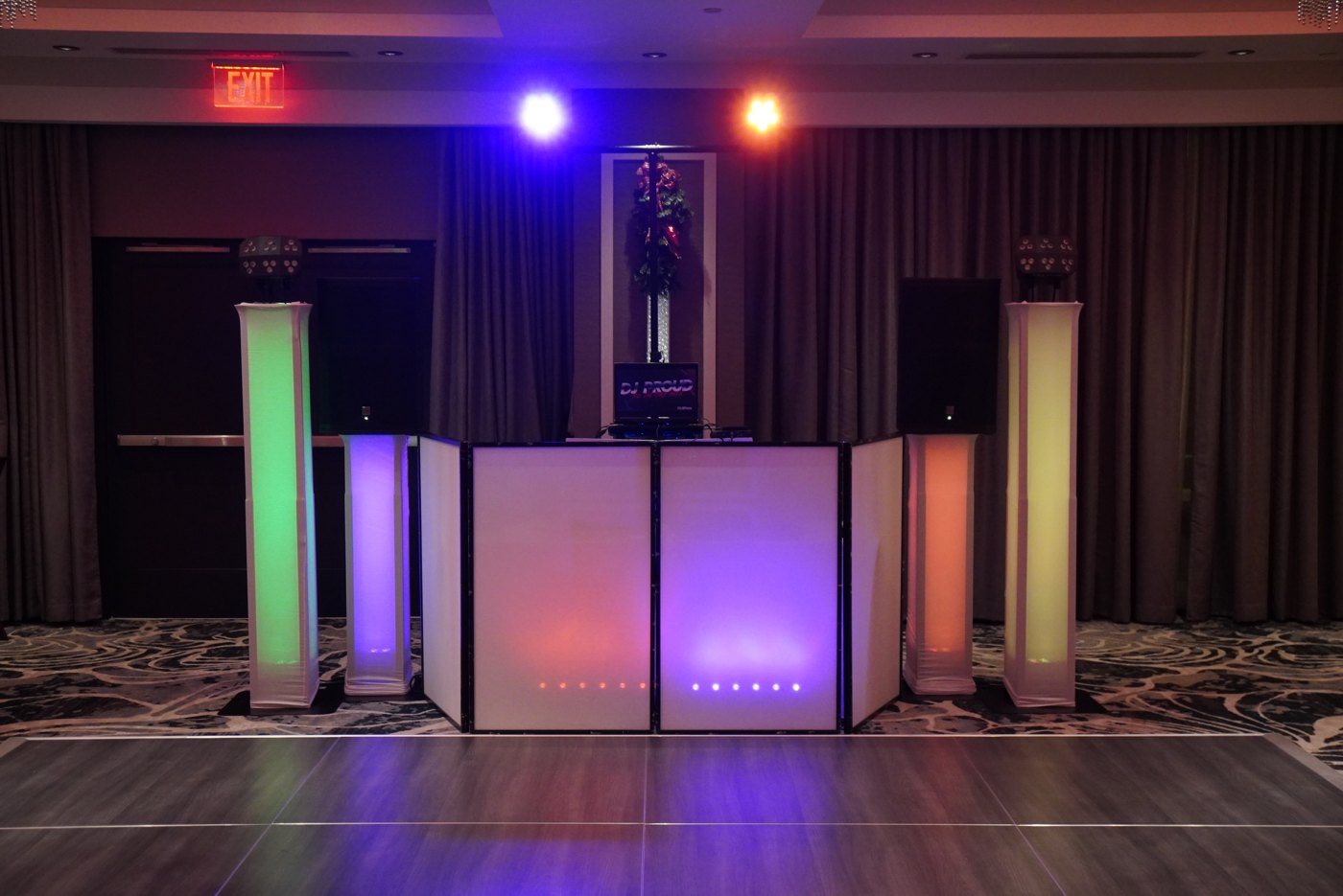 White DJ facade with uplight totems glowing green, blue and pink on an empty dance floor