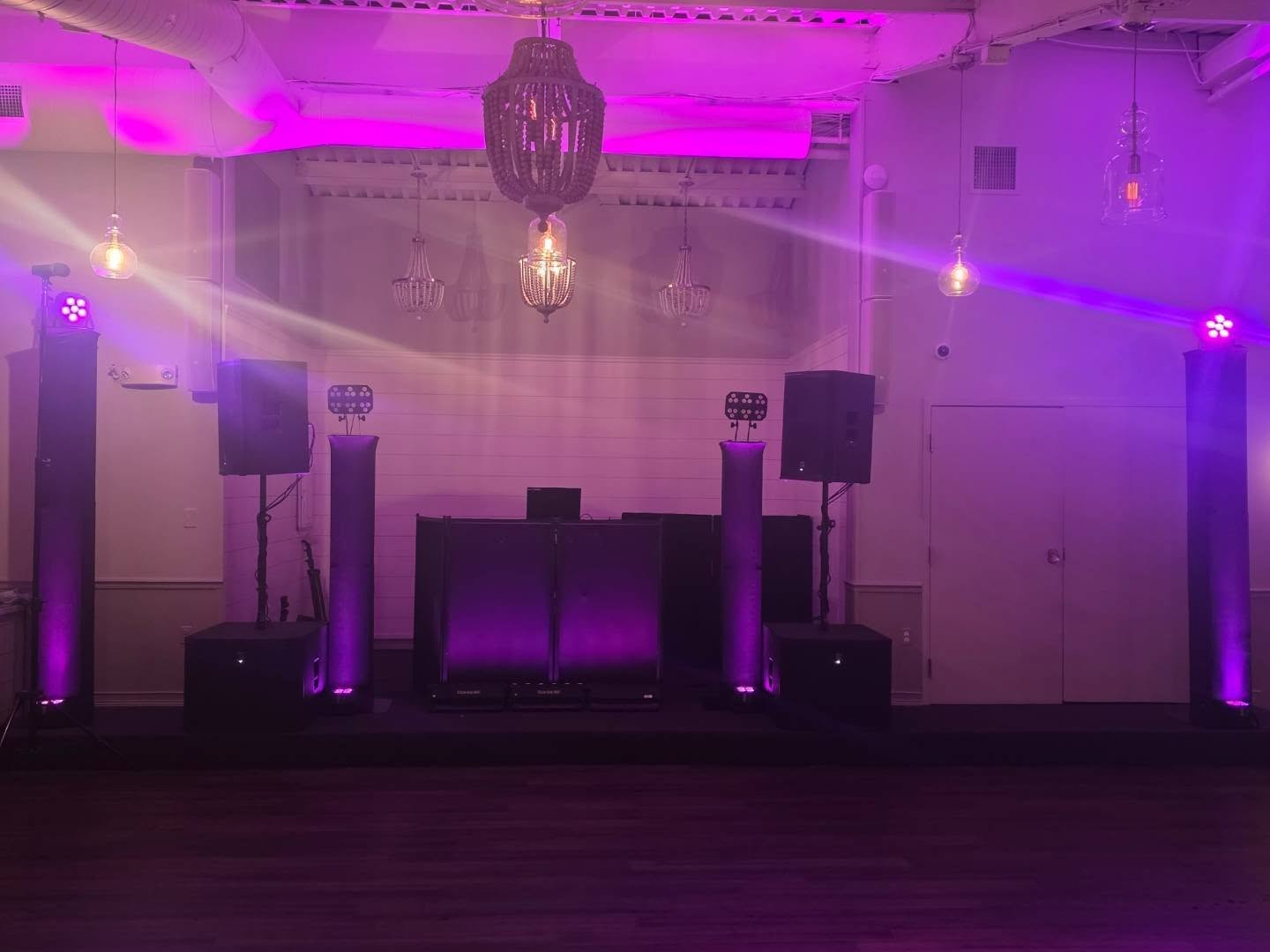 Full Proud Entertainment DJ setup at McLoone's Pier House — speakers, uplight totems and glowing facade under purple wash