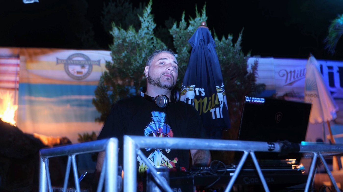 Barry at the decks at an outdoor night bar event, headphones around his neck