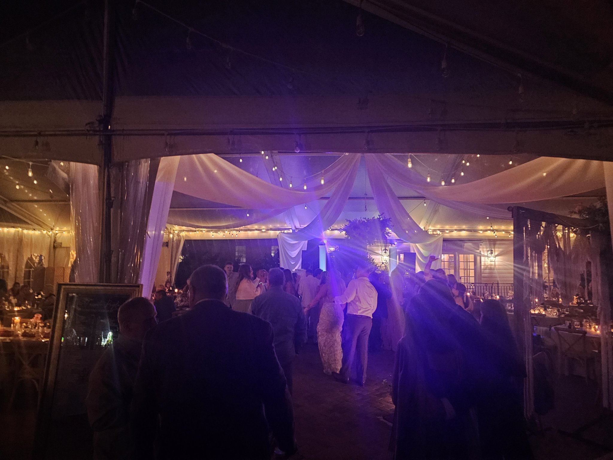 Tent wedding reception with purple uplighting, draped ceiling and a full dance floor