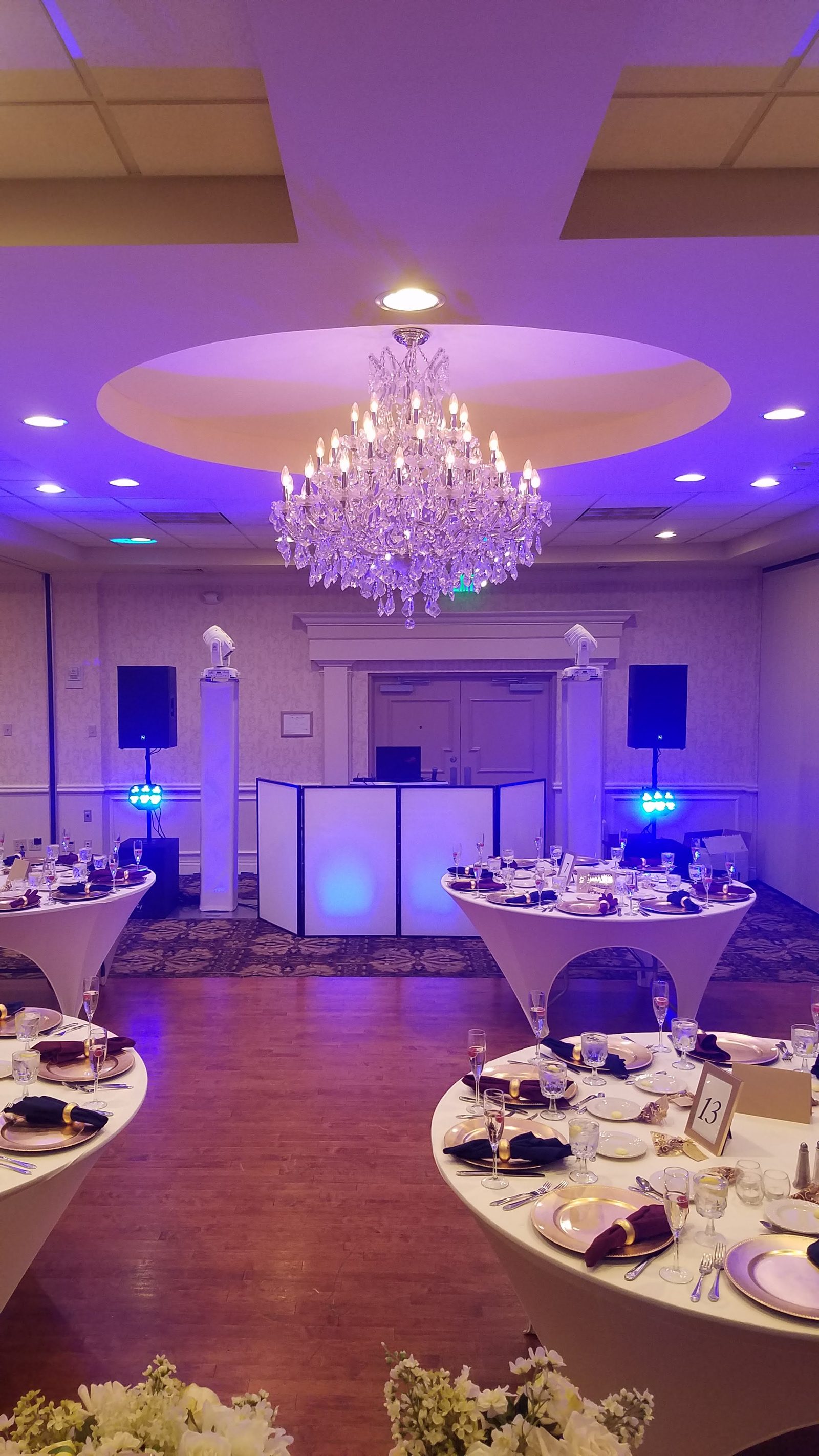 Grand ballroom with chandeliers and purple uplighting, set for a wedding