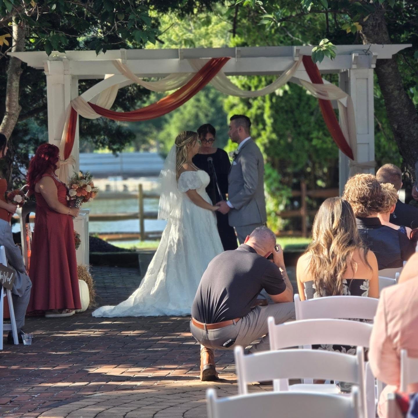 Outdoor wedding ceremony under a draped pergola — bride and groom with officiant
