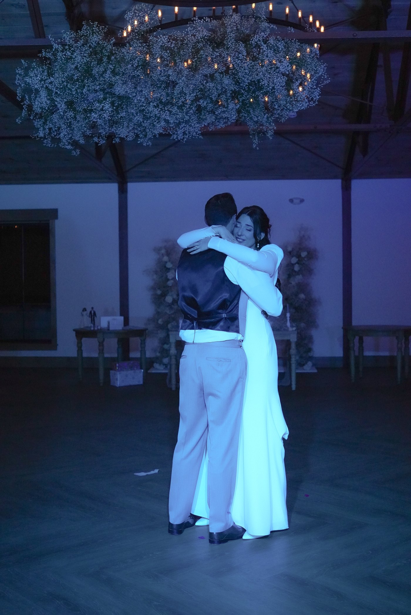 Bride and groom's first dance under blue uplighting and a floral chandelier