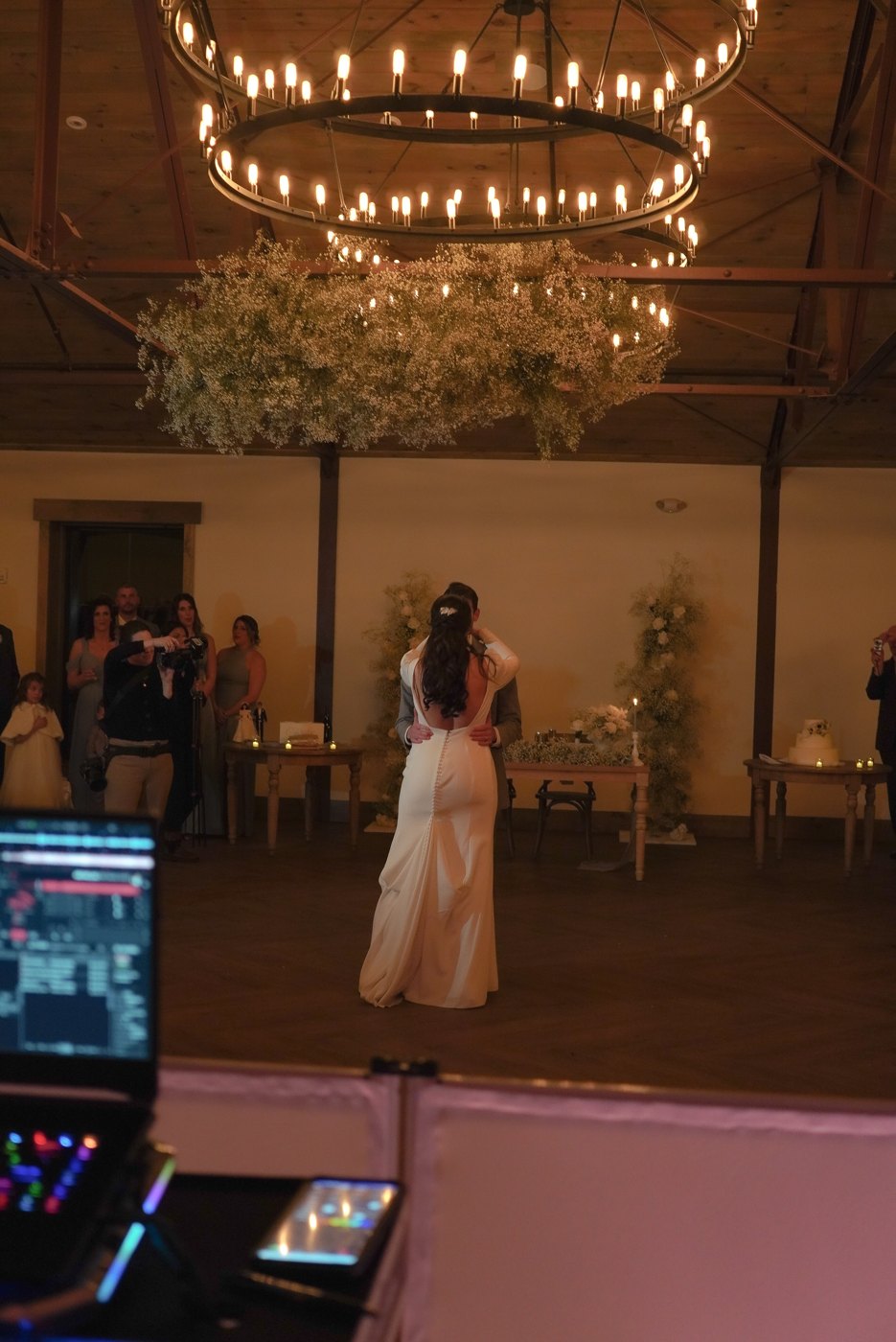 First dance seen from behind the DJ booth — couple under the candlelit chandelier