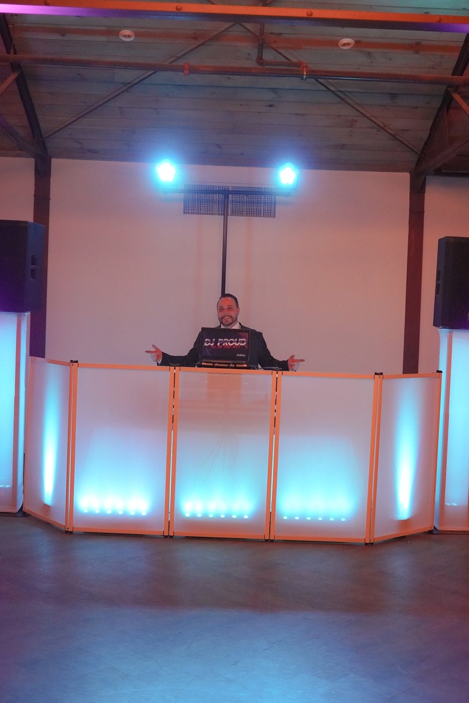 The white DJ facade glowing blue with DJ PROUD on the laptop screen, empty ballroom before the night