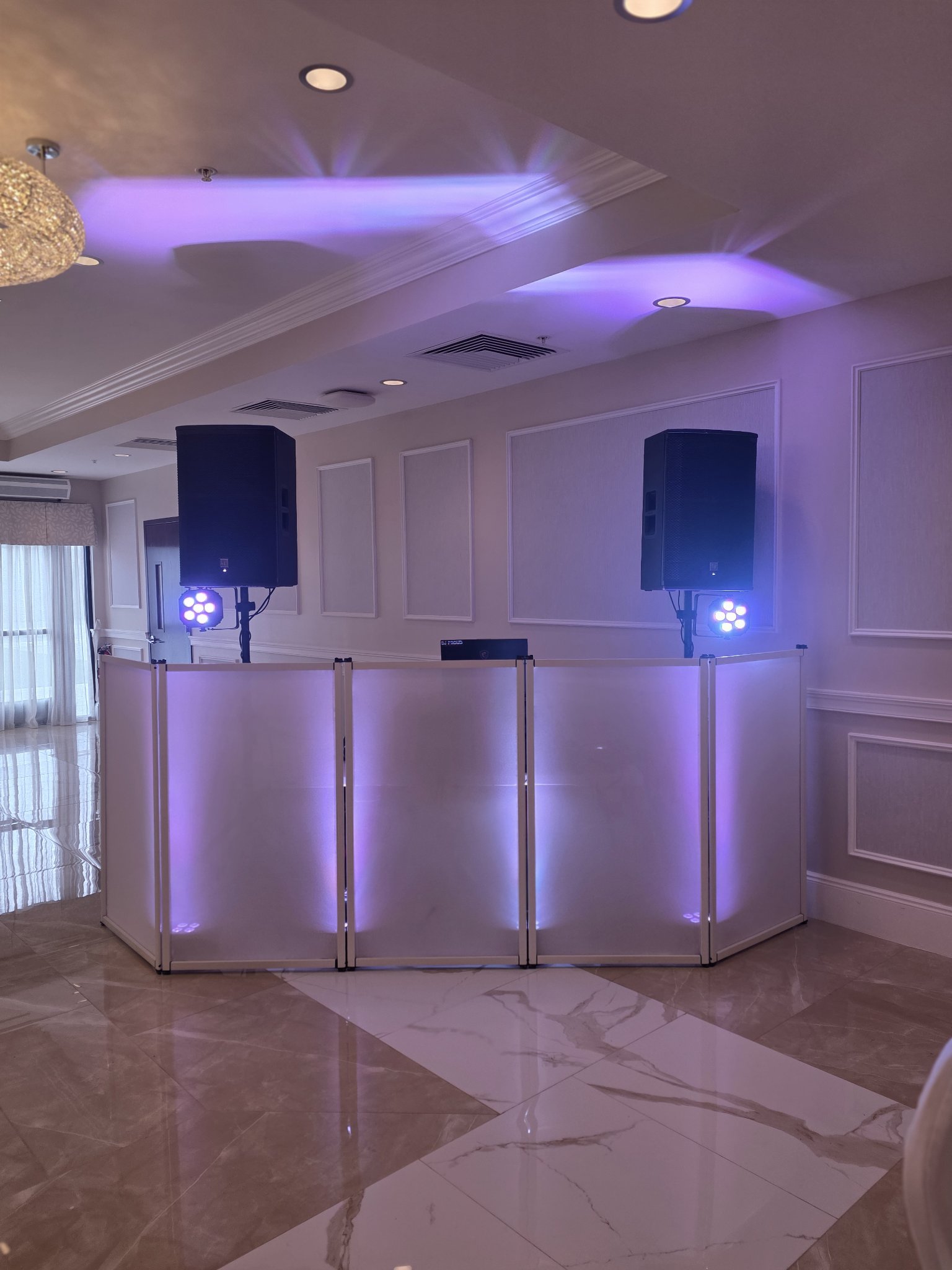 White glowing DJ facade with speakers and purple uplighting in a ballroom