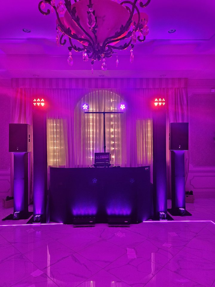 The Proudest black DJ setup with four purple up-lit towers in a chandelier ballroom